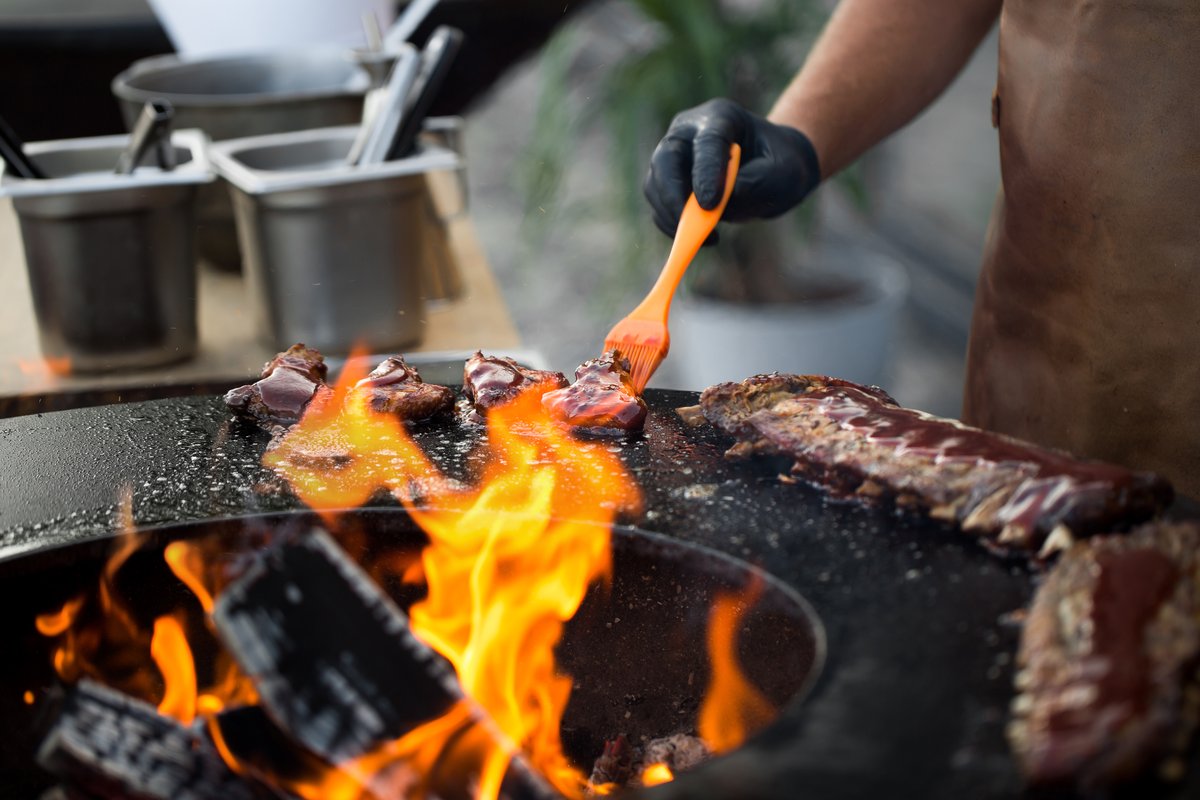Vlees wordt bestreken met saus op de grillplaat boven open vuur