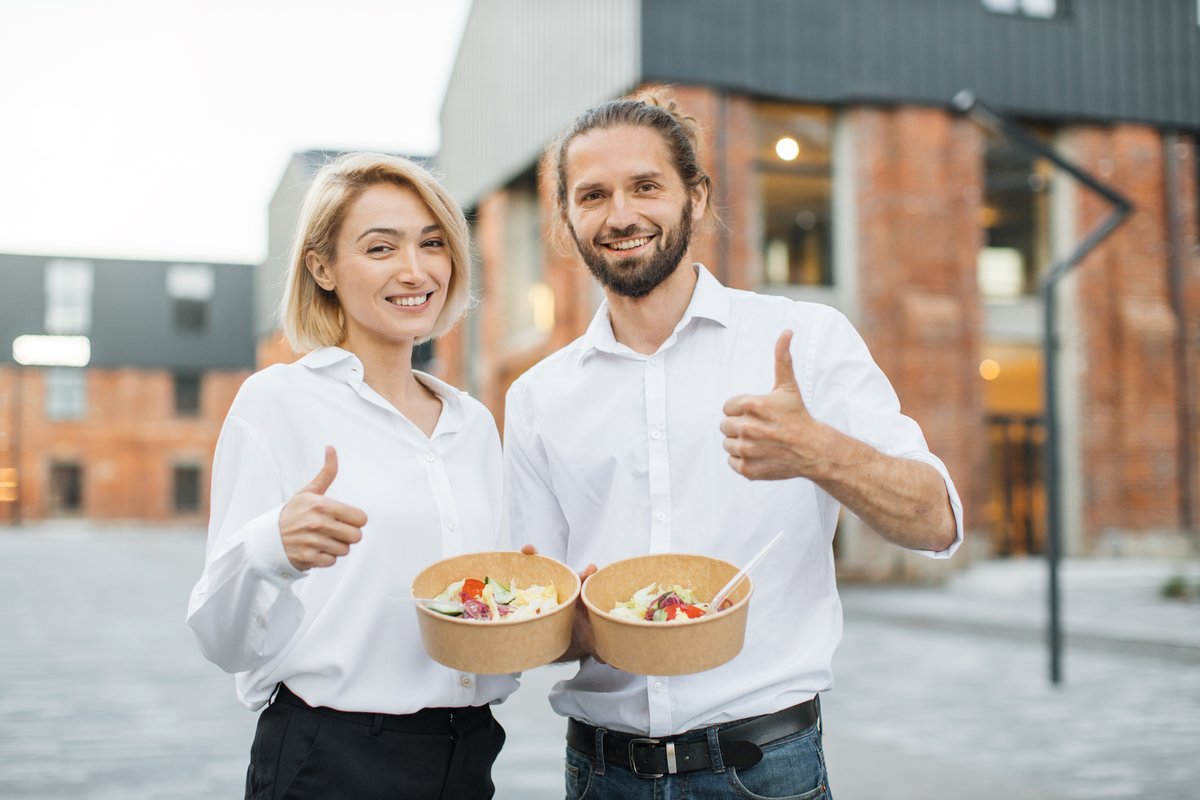 Twee collega's van Vers Catering steken duim omhoog bij het uitdelen van saladebowls